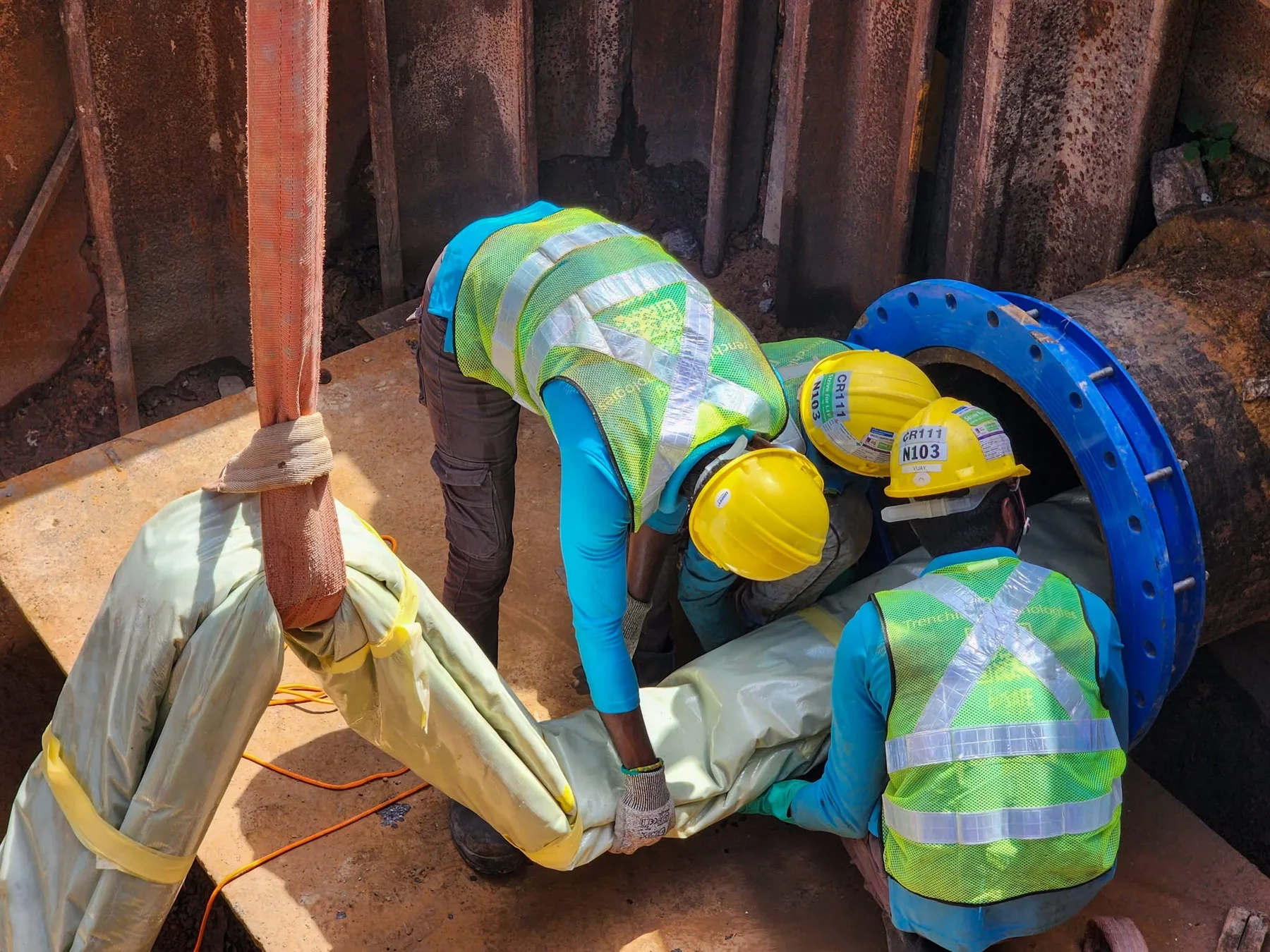 Workers guiding a liner into a large industrial pipe